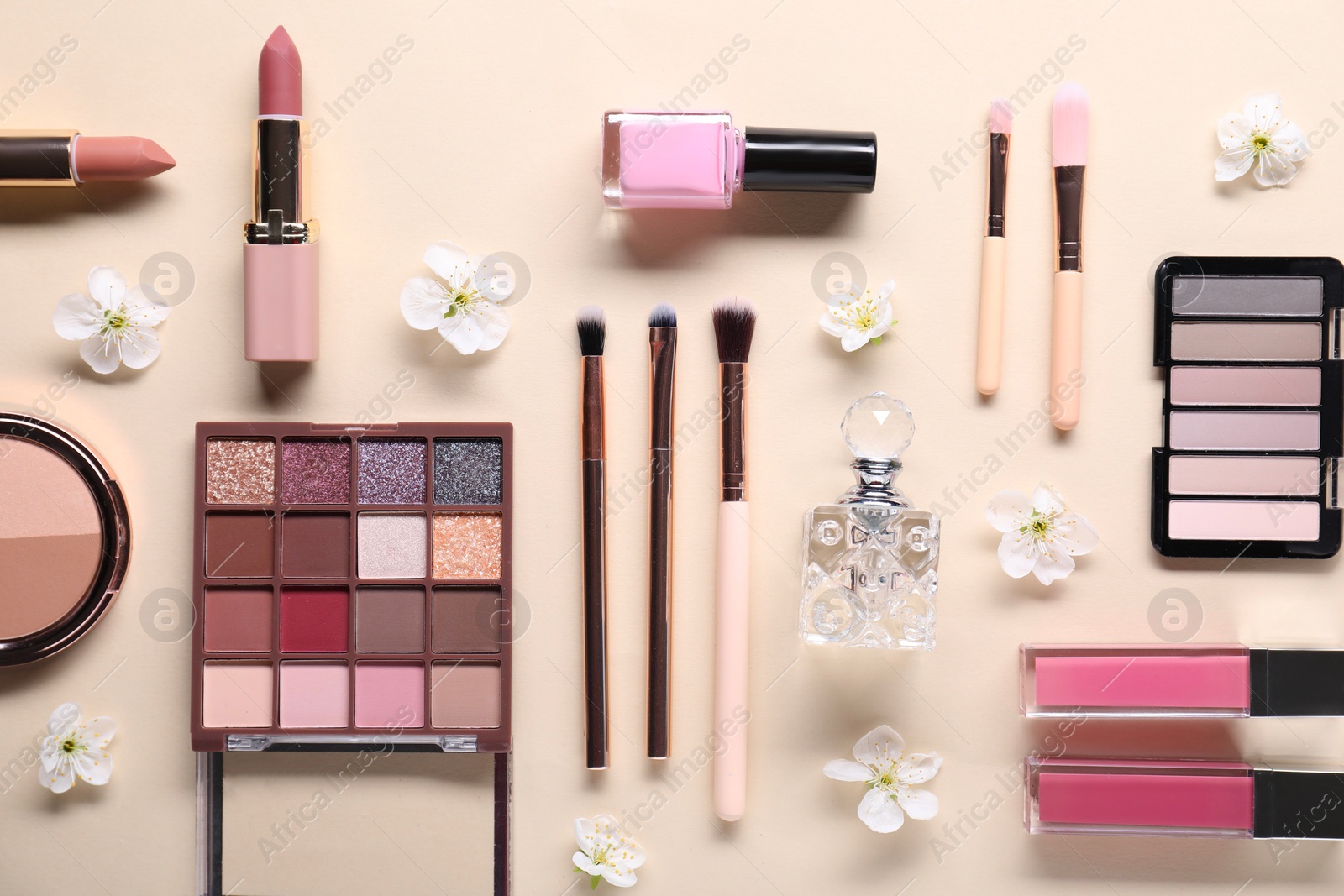 Photo of Flat lay composition with different makeup products and beautiful spring flowers on beige background