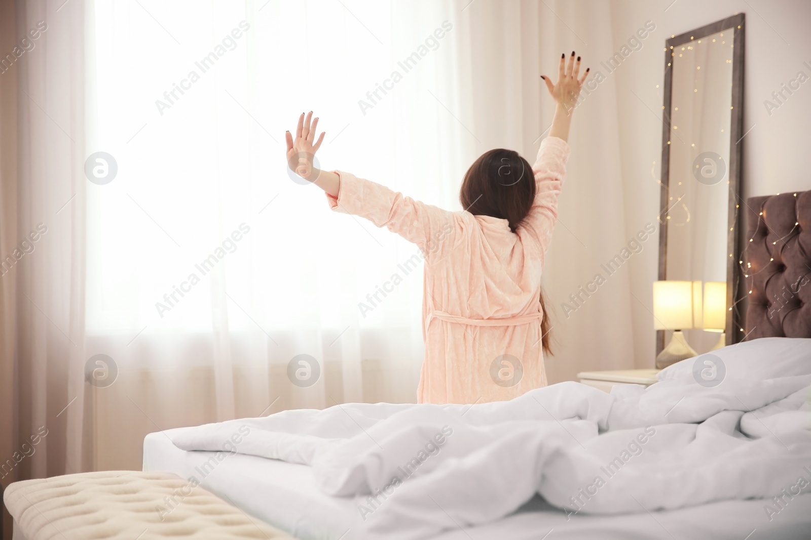 Photo of Young woman stretching on bed in hotel room