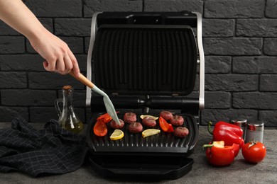 Photo of Woman cooking meat balls with bell peppers and lemon on electric grill at grey textured table, closeup