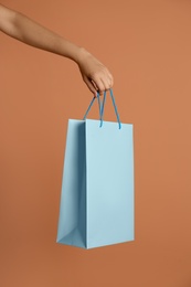 Photo of Woman holding paper shopping bag on light brown background, closeup