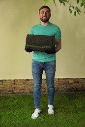 Photo of Young man holding rolled grass sod at backyard