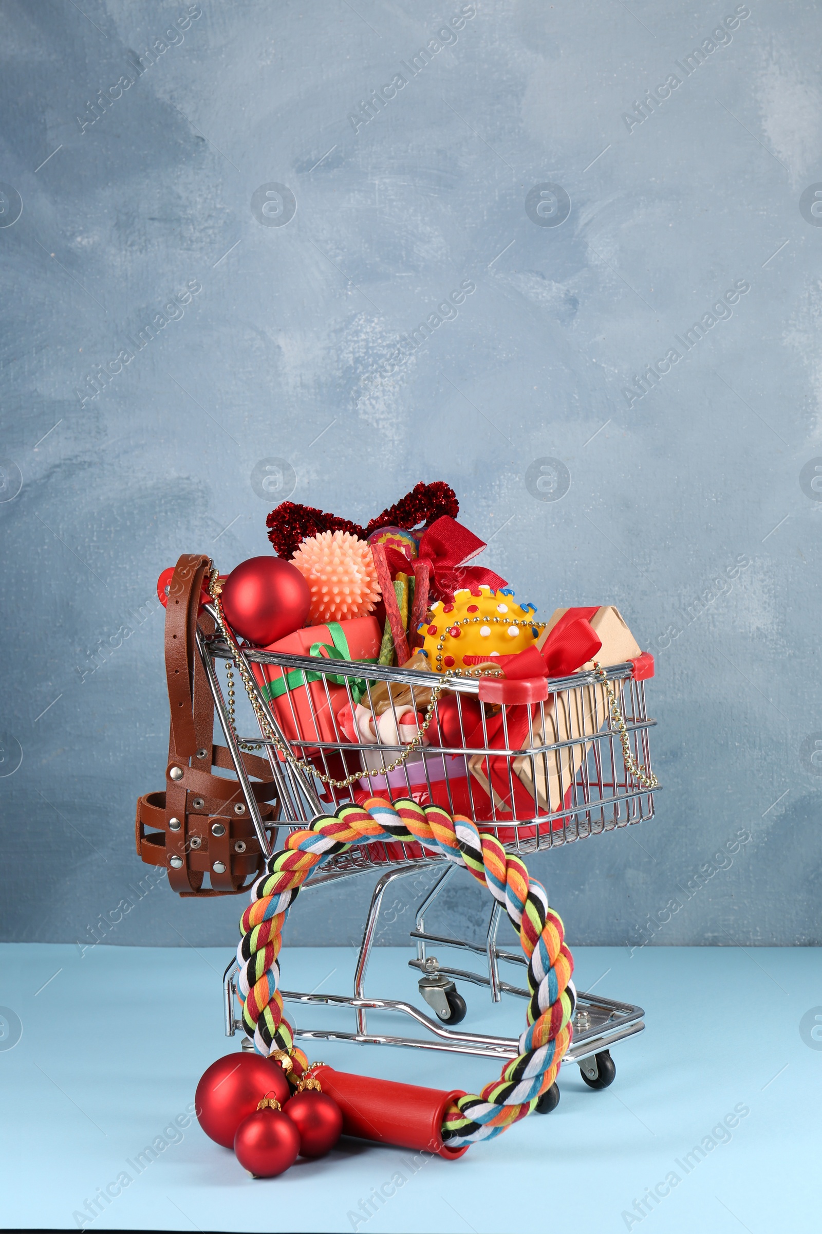 Photo of Small shopping cart with different pet goods and Christmas gifts on light blue background. Shop assortment