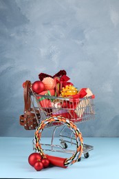 Small shopping cart with different pet goods and Christmas gifts on light blue background. Shop assortment