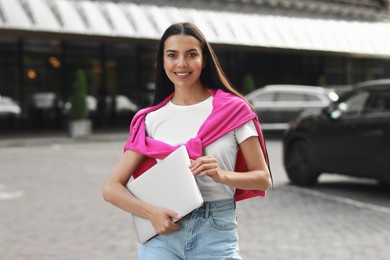 Photo of Happy young woman holding modern laptop on city street