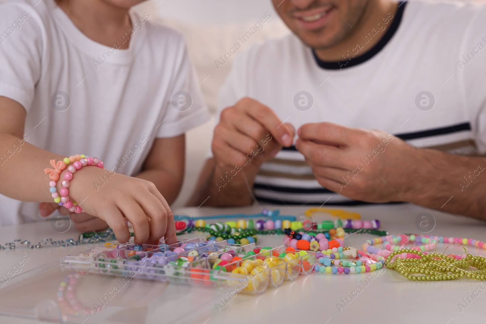 Photo of Father with his daughter making beaded jewelry at table, closeup