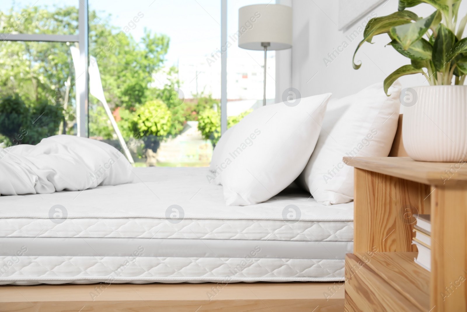 Photo of Wooden bed with soft white mattress, blanket and pillows in cozy room interior