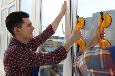 Photo of Workers using suction lifters during plastic window installation indoors