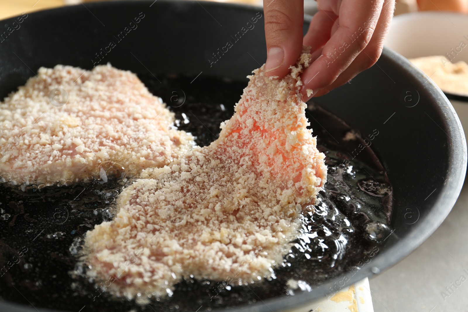 Photo of Cooking schnitzel. Woman putting raw pork chop in bread crumbs into frying pan, closeup