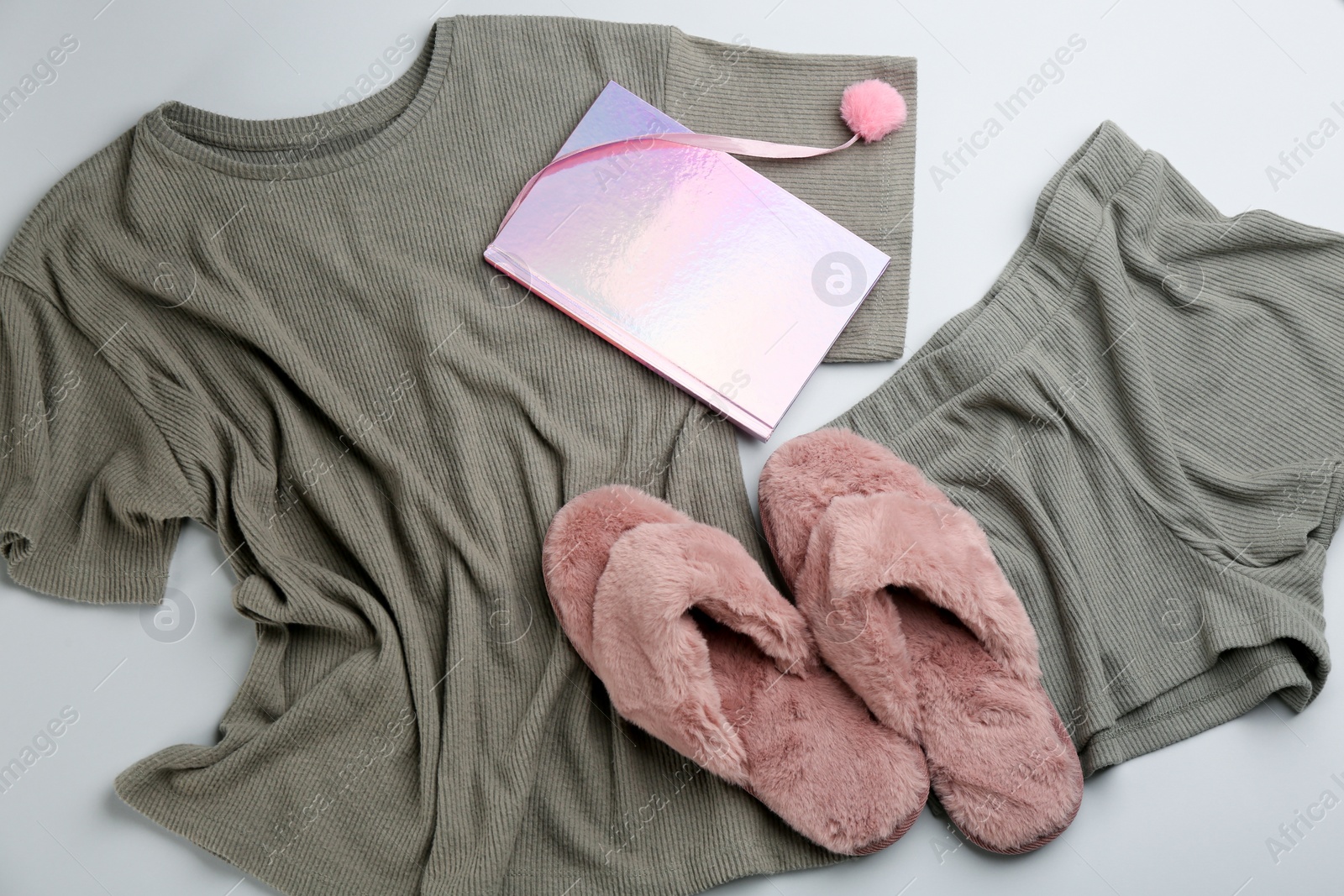 Photo of Pair of fluffy slippers, pajamas and notebook on grey background, flat lay. Comfortable home outfit