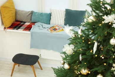 Photo of Beautiful Christmas tree near cozy window sill with pillows in room. Interior design