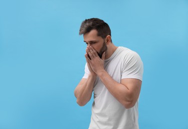 Photo of Man sneezing on light blue background. Cold symptoms