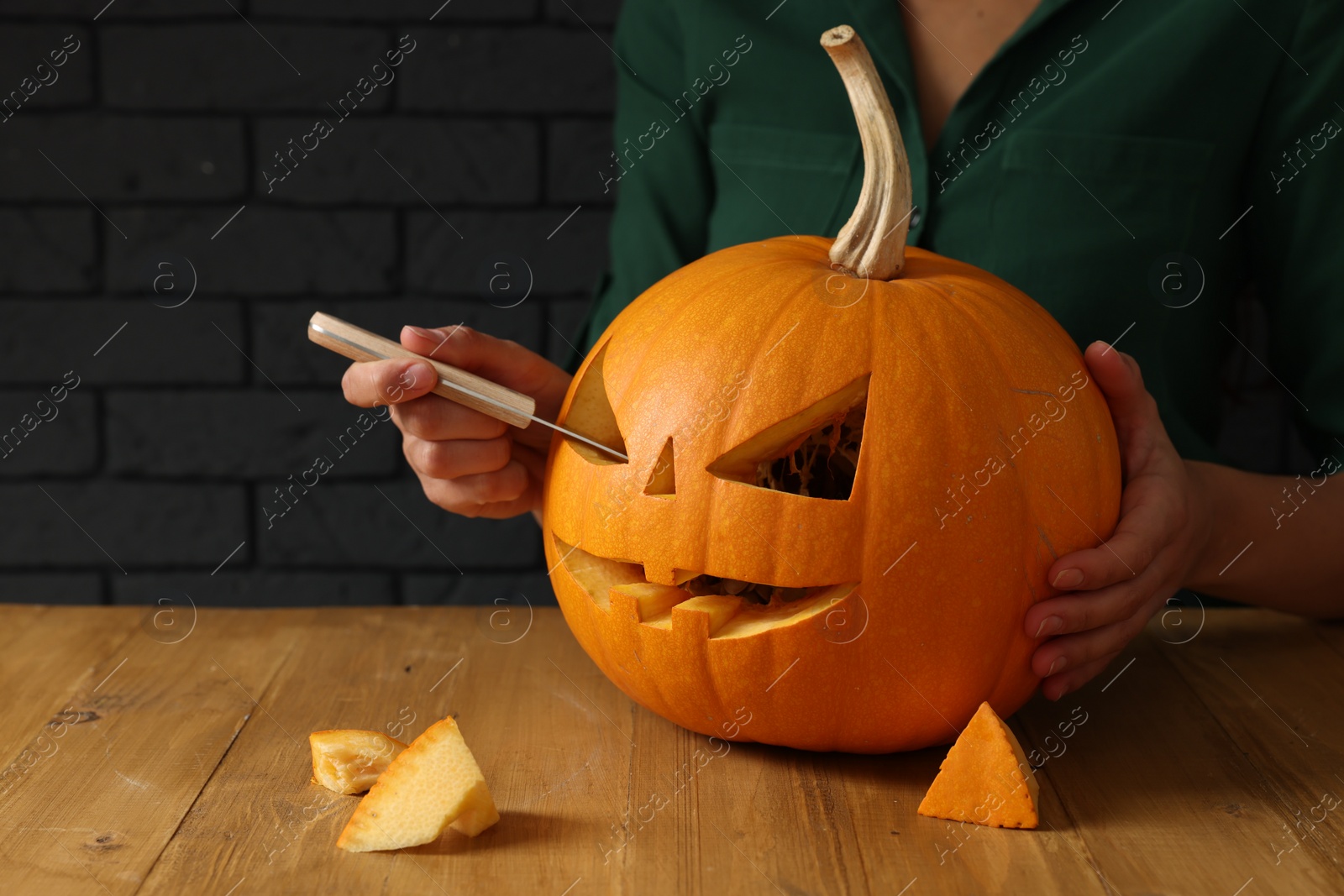 Photo of Woman carving pumpkin at wooden table, closeup. Halloween celebration