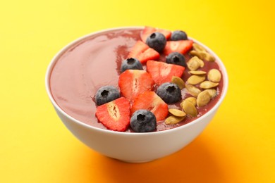 Photo of Bowl of delicious smoothie with fresh blueberries, strawberries and pumpkin seeds on yellow background, closeup