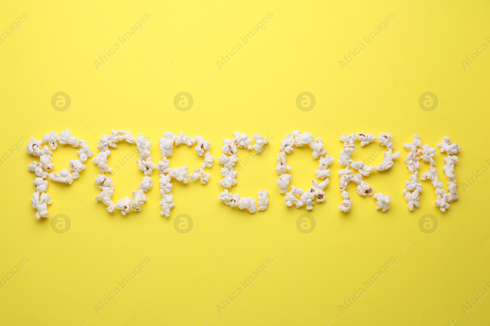 Photo of Word Popcorn made of tasty ingredients on yellow background, top view
