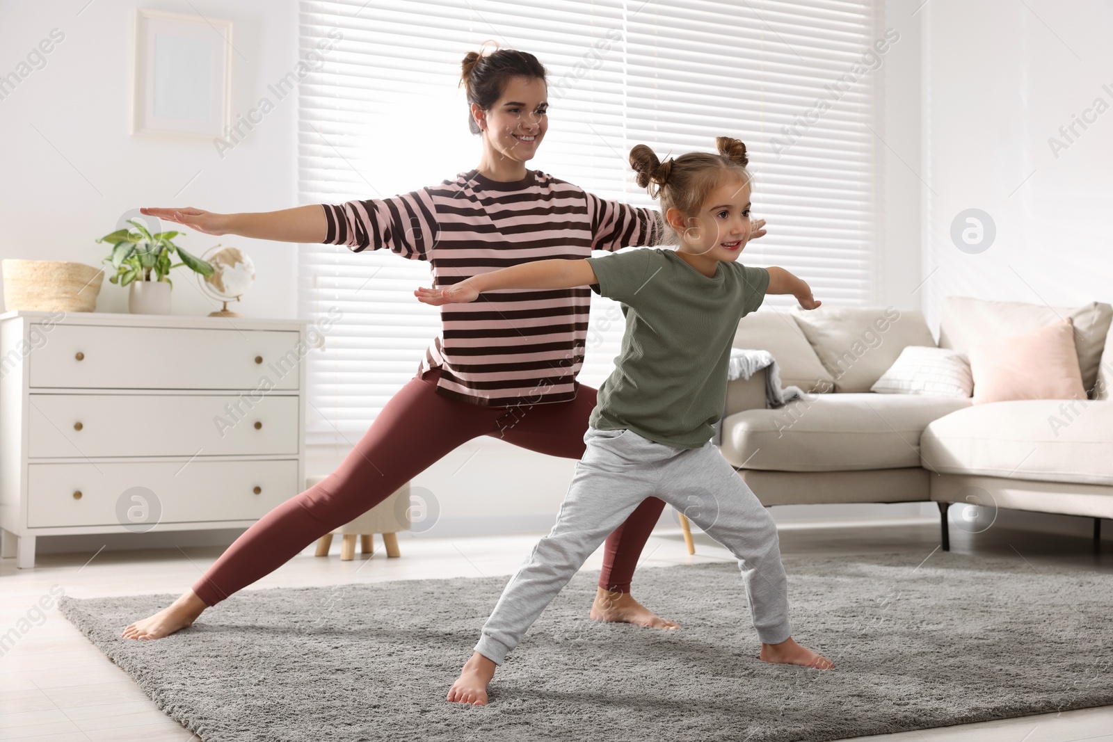 Photo of Young mother and her daughter practicing yoga together at home