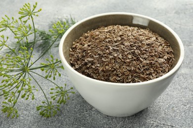 Photo of Bowl of dry seeds and fresh dill on grey table, closeup