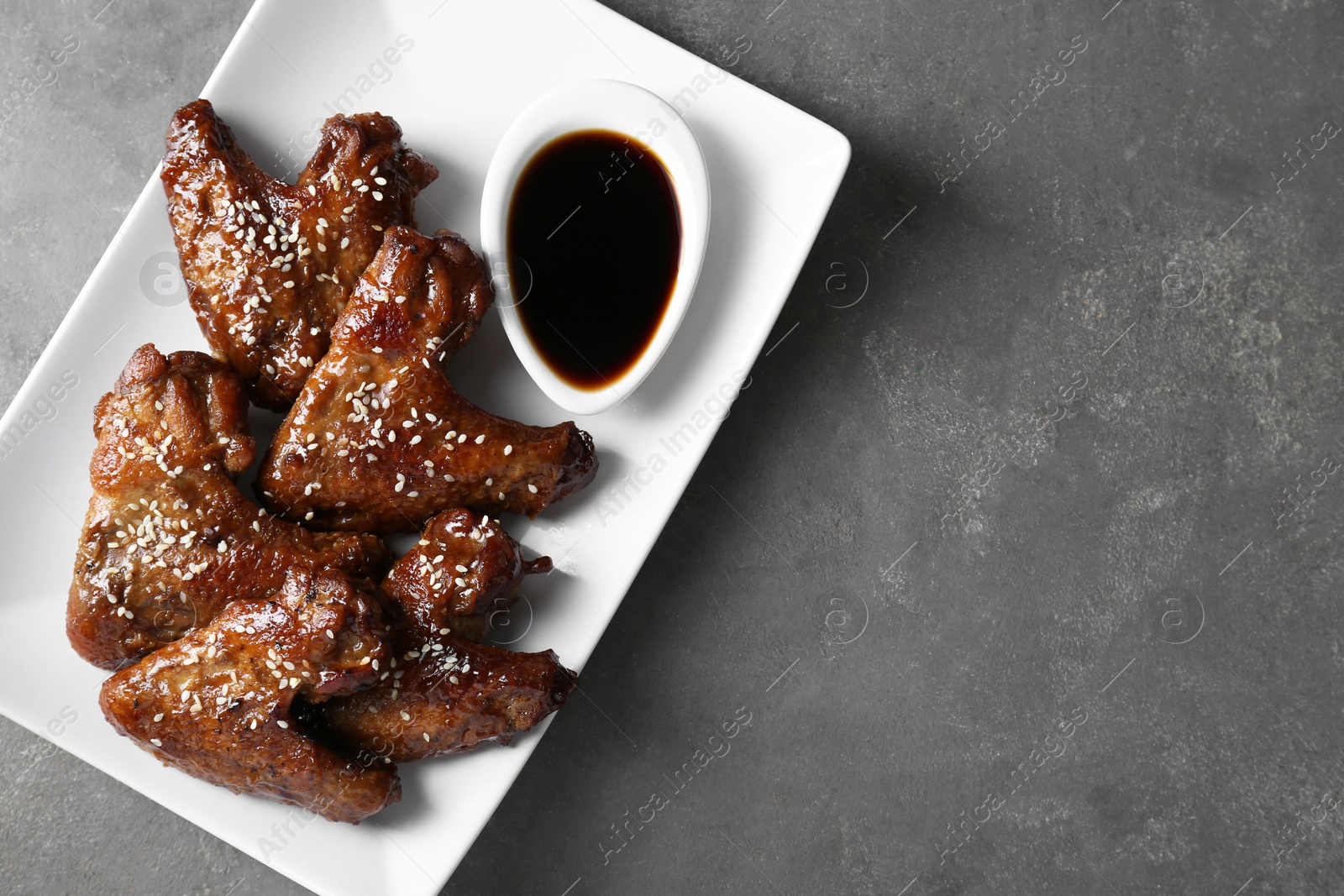 Photo of Glazed chicken wings and soy sauce on grey table, top view. Space for text