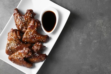 Glazed chicken wings and soy sauce on grey table, top view. Space for text