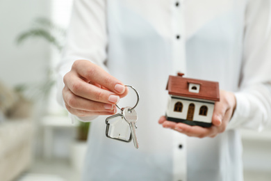 Photo of Real estate agent holding house model and key indoors, closeup