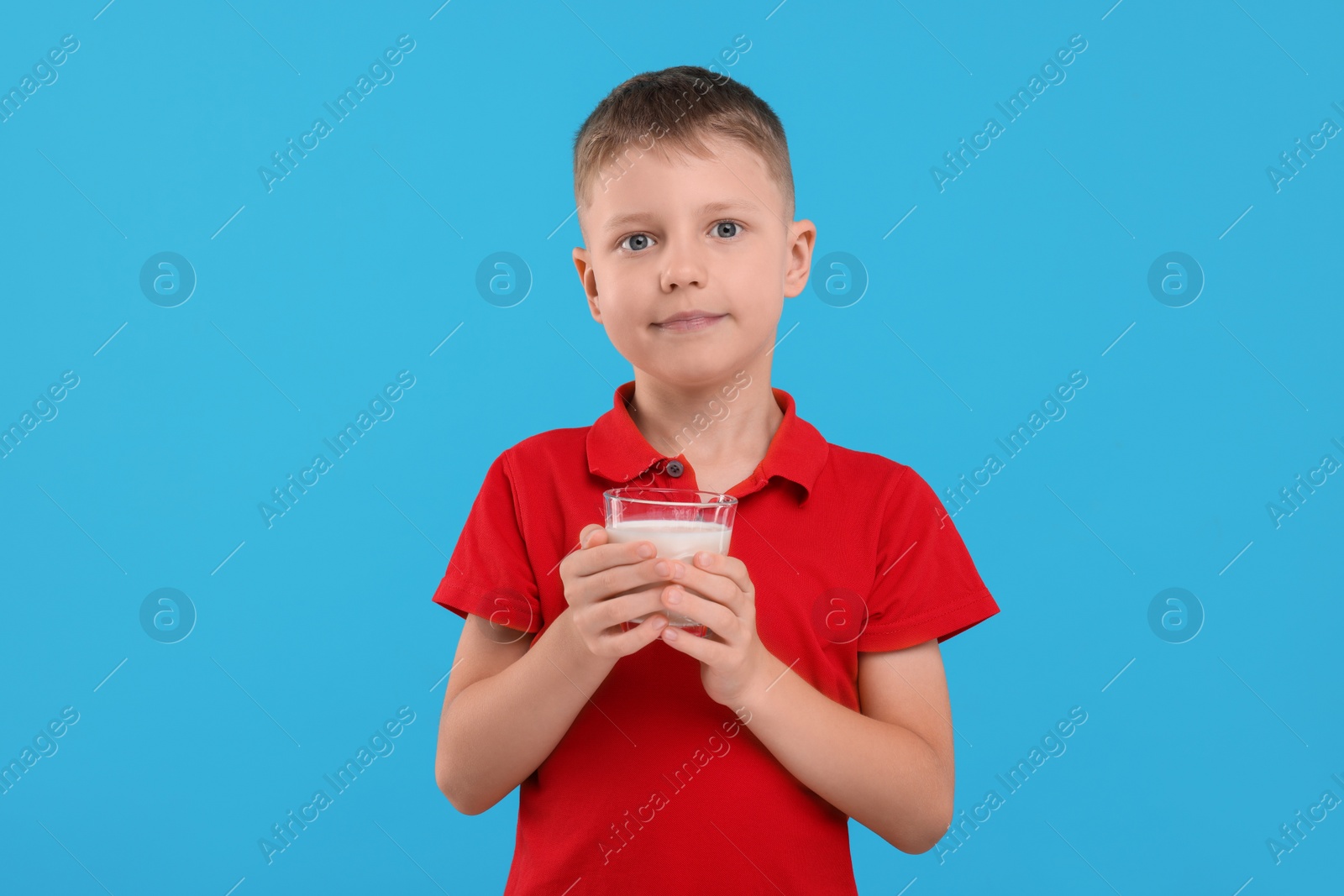Photo of Cute boy with glass of fresh milk on light blue background