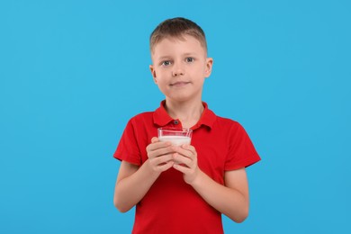 Cute boy with glass of fresh milk on light blue background