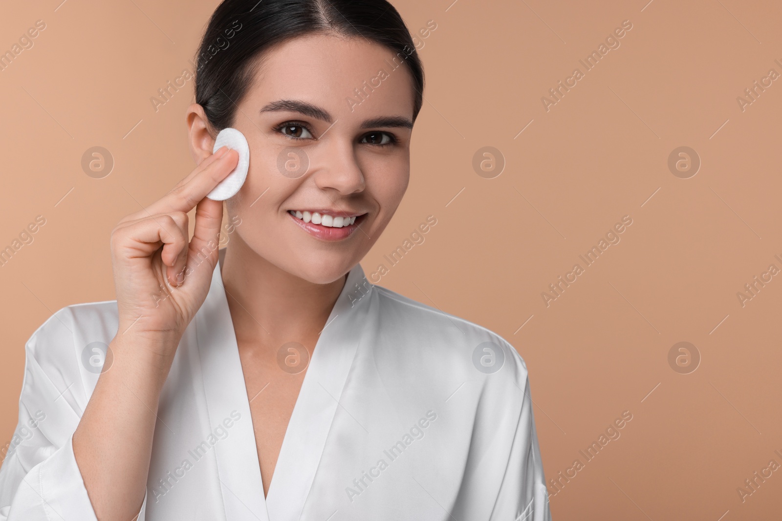 Photo of Young woman cleaning her face with cotton pad on beige background. Space for text