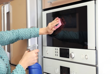 Photo of Woman cleaning oven with sponge in kitchen