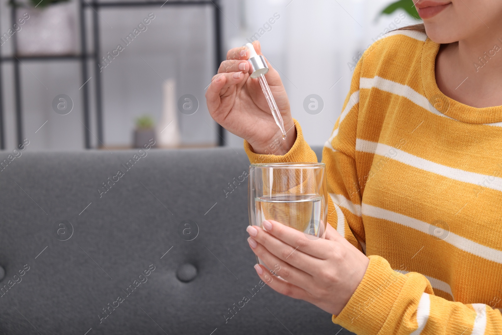 Photo of Woman dripping food supplement into glass of water indoors, closeup. Space for text