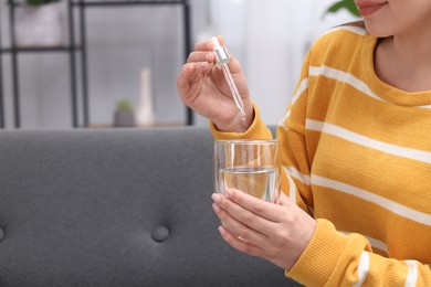 Photo of Woman dripping food supplement into glass of water indoors, closeup. Space for text