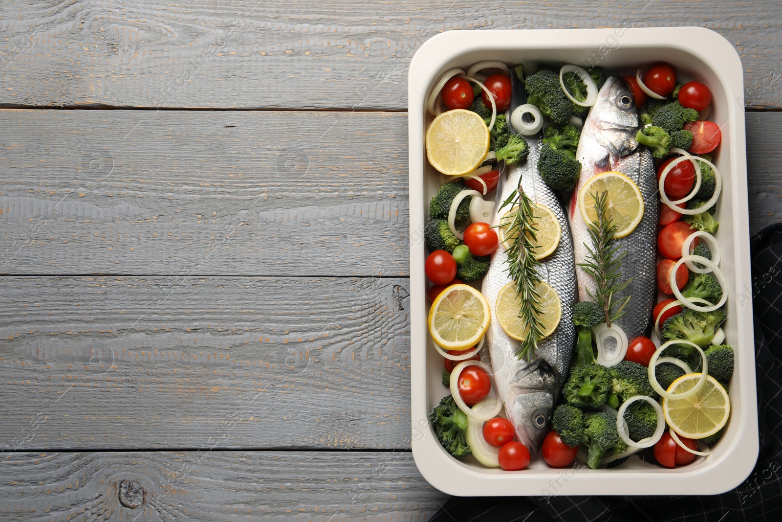 Photo of Raw fish with vegetables and lemon in baking dish on grey wooden table, top view. Space for text