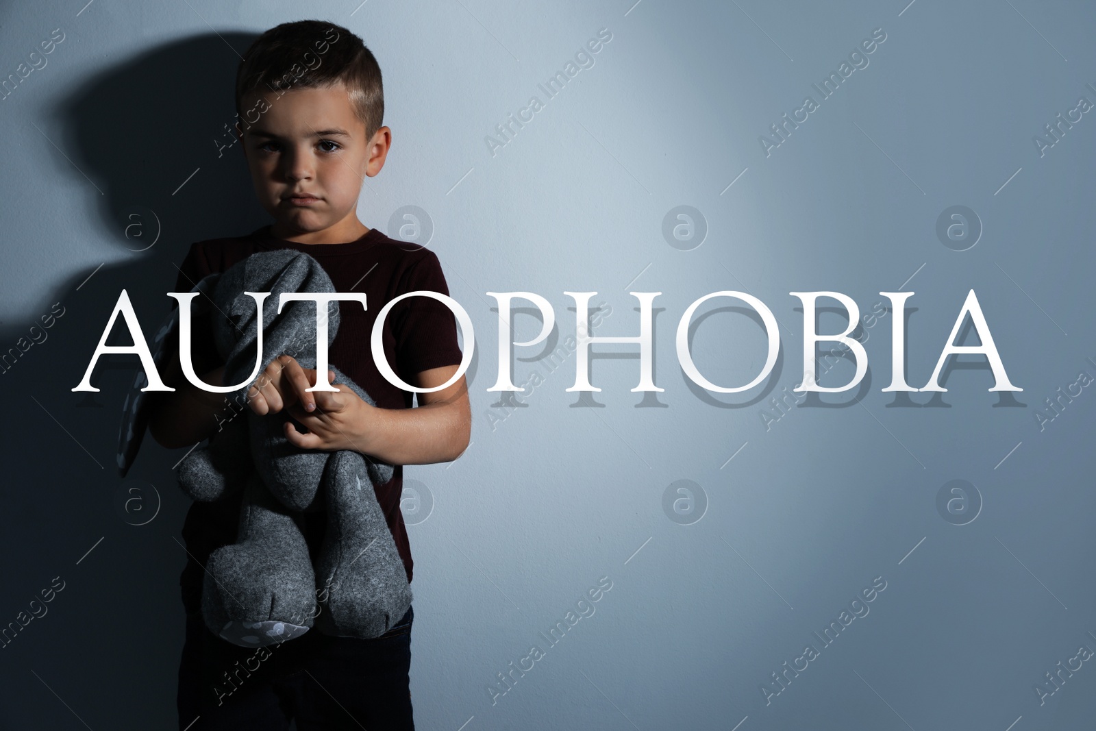 Image of Sad little boy with toy near light wall. Autophobia - fear of isolation