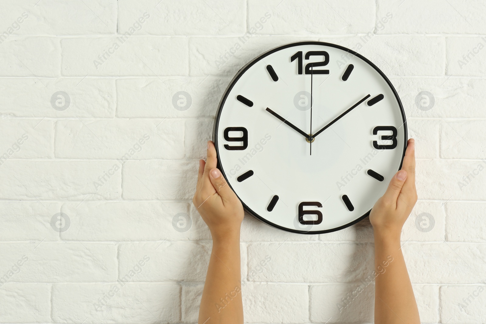Photo of Woman touching clock on white brick wall, space for text. Time management