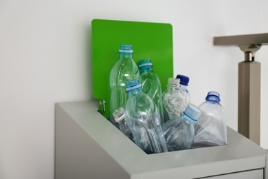 Photo of Many used plastic bottles in metal bin indoors, closeup. Recycling problem