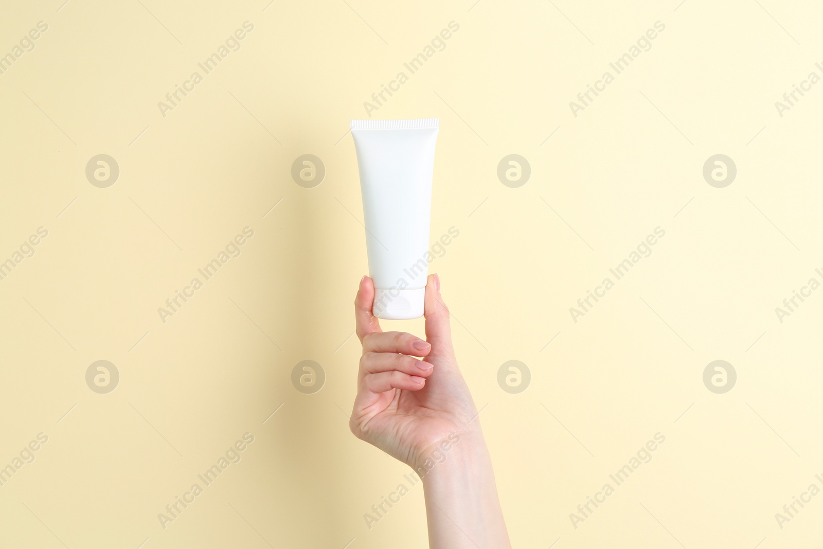 Photo of Woman holding tube of cream on yellow background, closeup