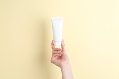 Woman holding tube of cream on yellow background, closeup