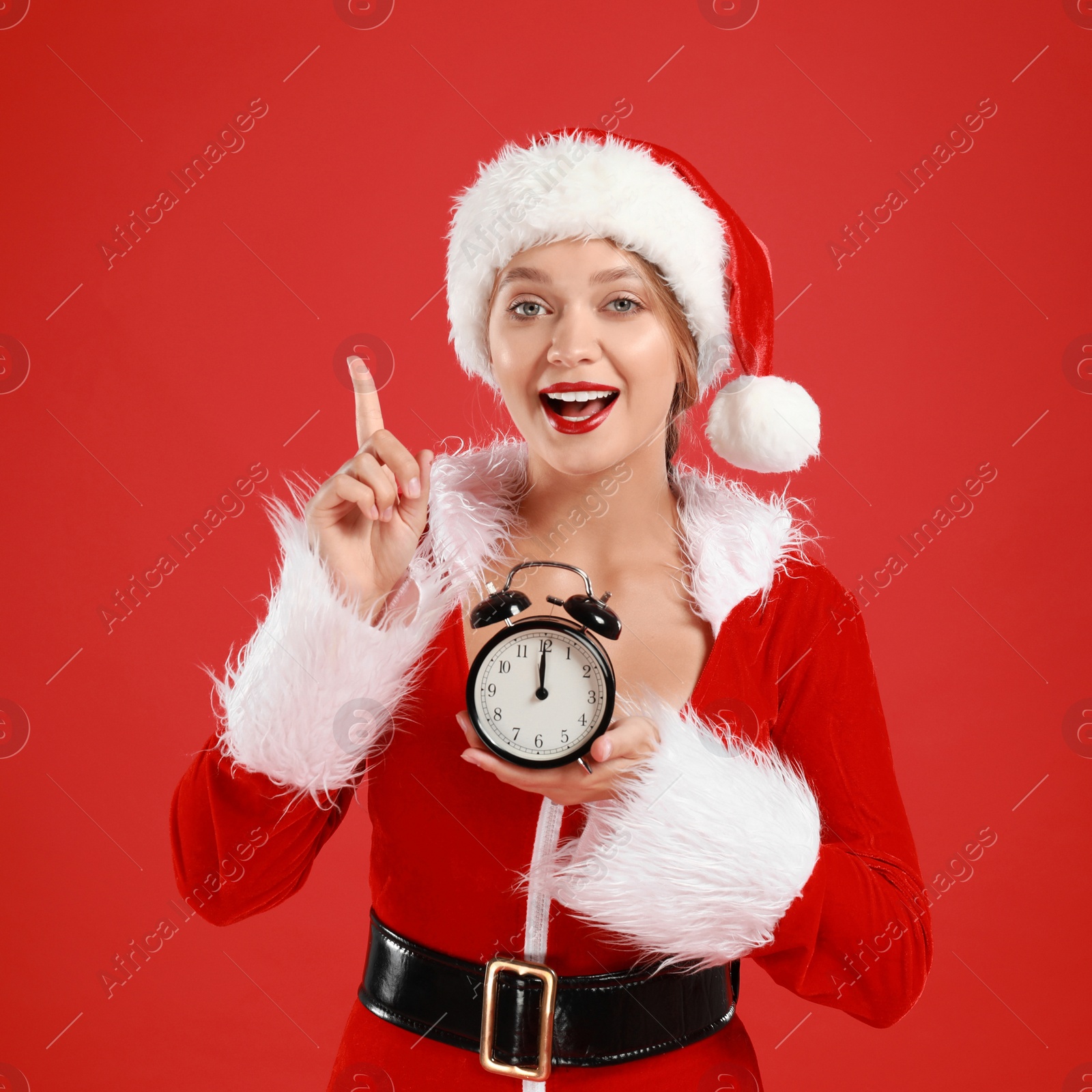 Photo of Beautiful Santa girl with alarm clock on red background. Christmas eve