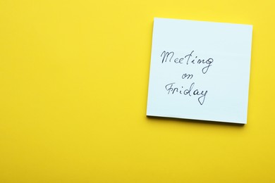 Photo of Paper note with words Meeting on Friday against yellow background, top view. Space for text