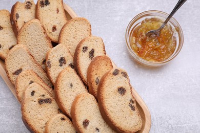 Photo of Sweet hard chuck crackers with raisins and jam on light grey table, flat lay