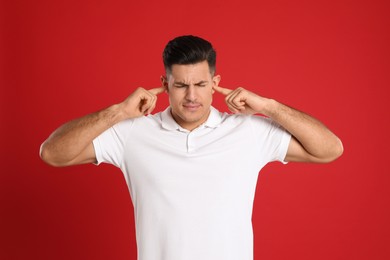 Photo of Man covering ears with fingers on red background