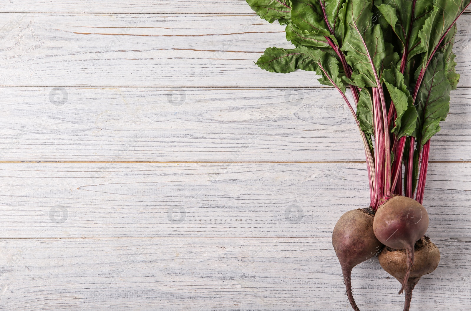 Photo of Bunch of fresh beets with leaves on white wooden table, top view. Space for text