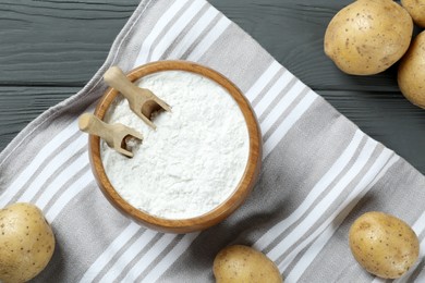 Photo of Bowl with starch, scoops and fresh potatoes on grey wooden table, flat lay