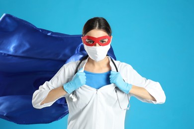 Photo of Doctor dressed as superhero posing on light blue background. Concept of medical workers fighting with COVID-19