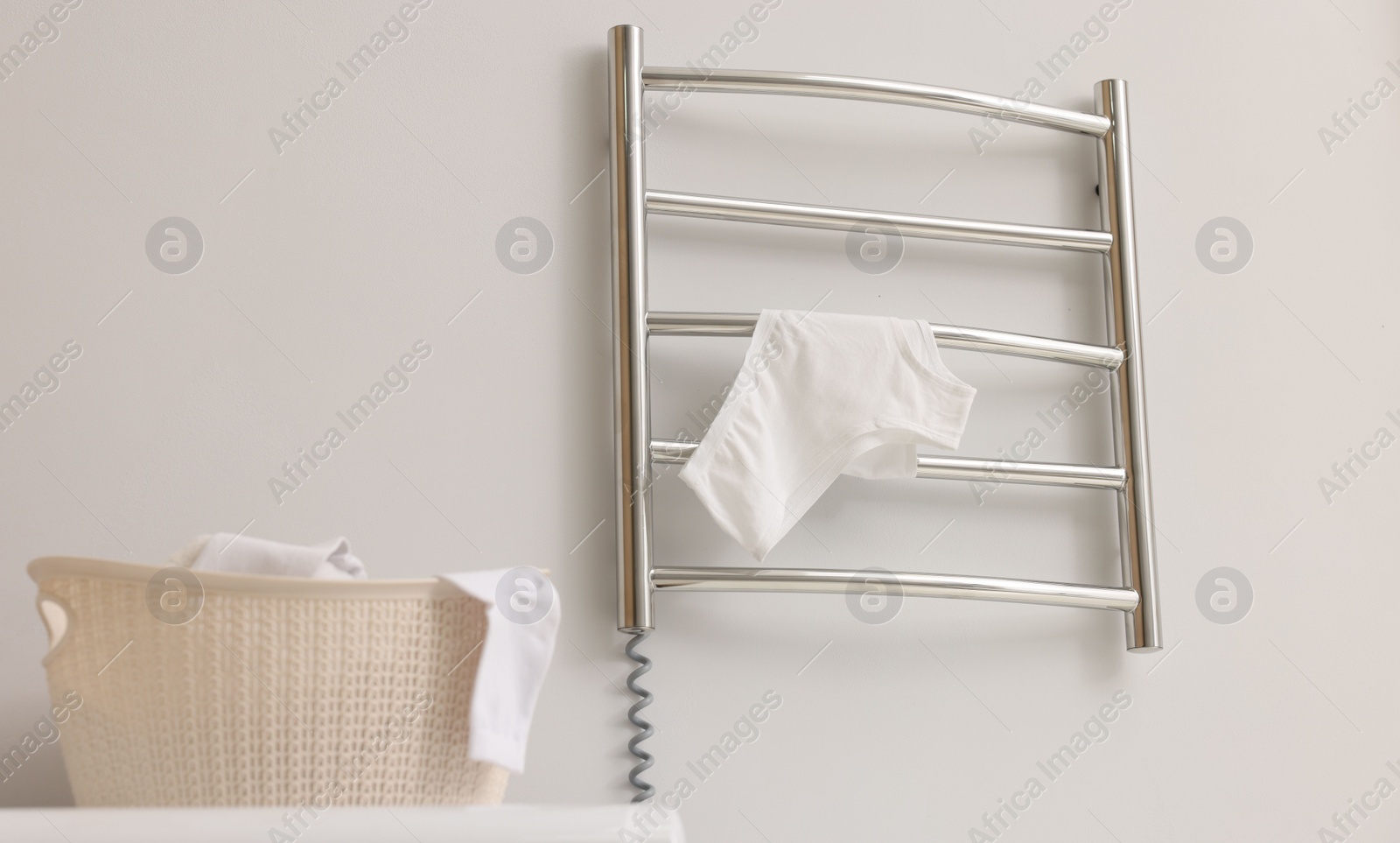Photo of Heated towel rail with underwear on white wall in bathroom