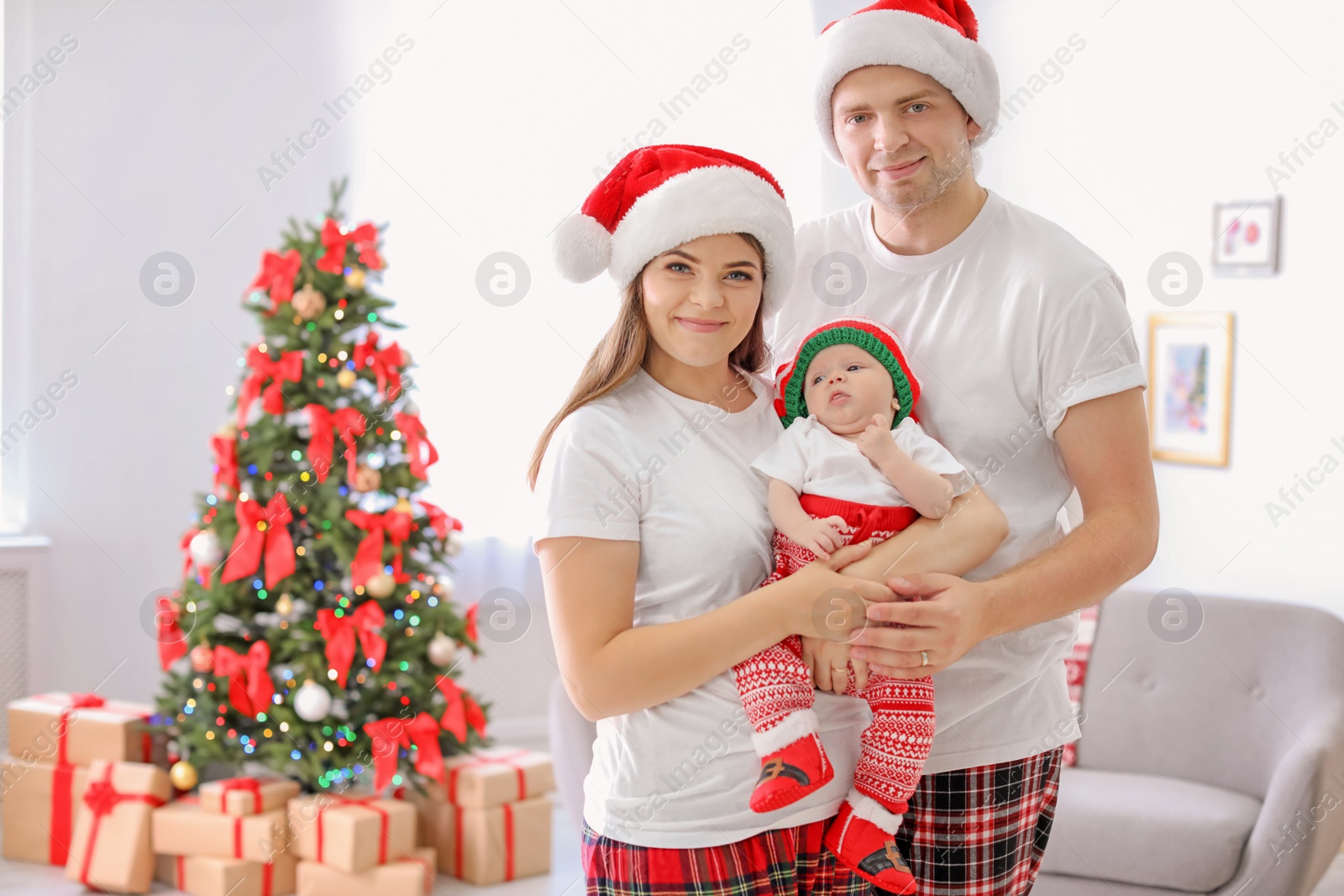 Photo of Happy couple with baby in Christmas hats at home