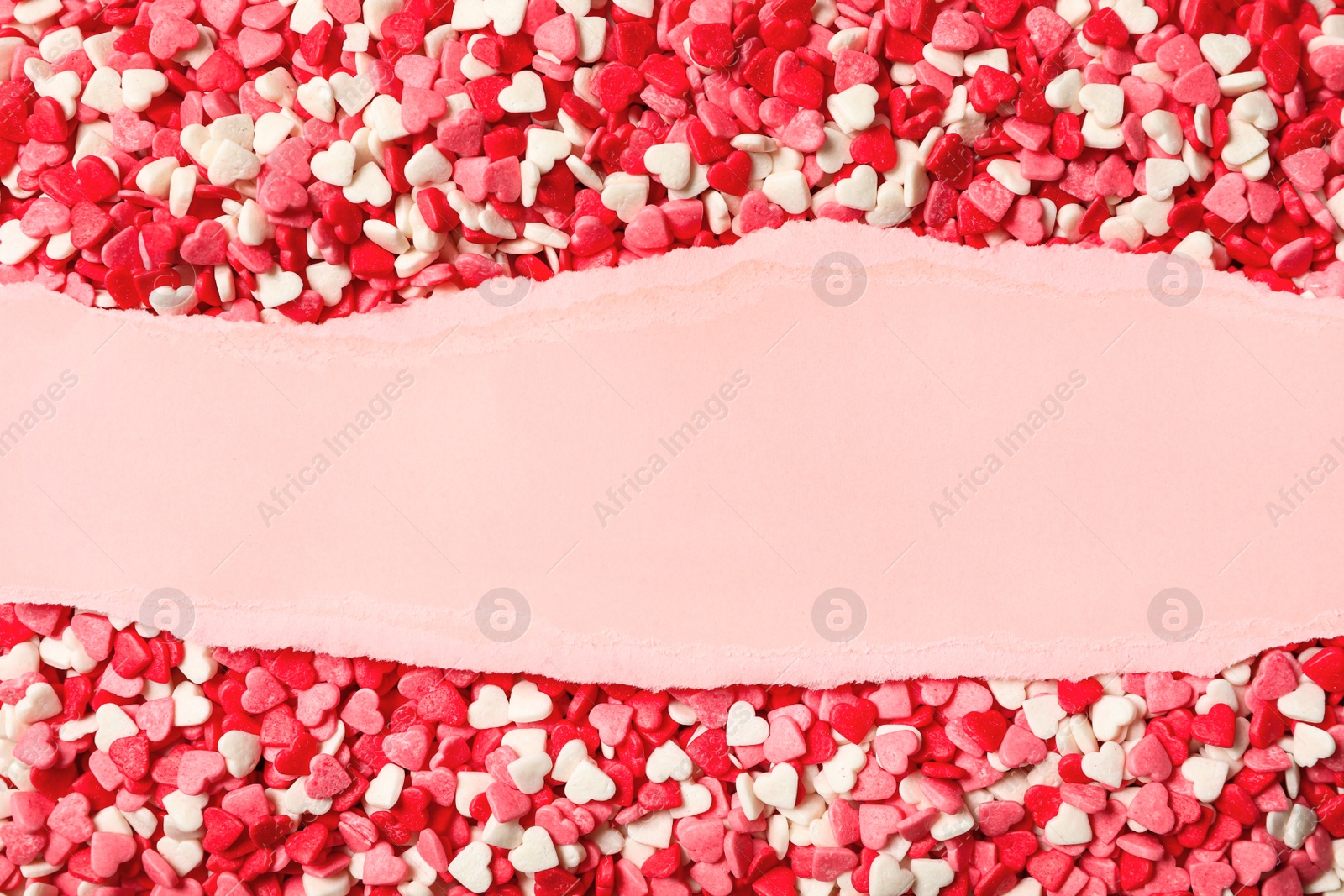 Photo of Blank torn paper on pile of color heart shaped sprinkles, top view. Space for text