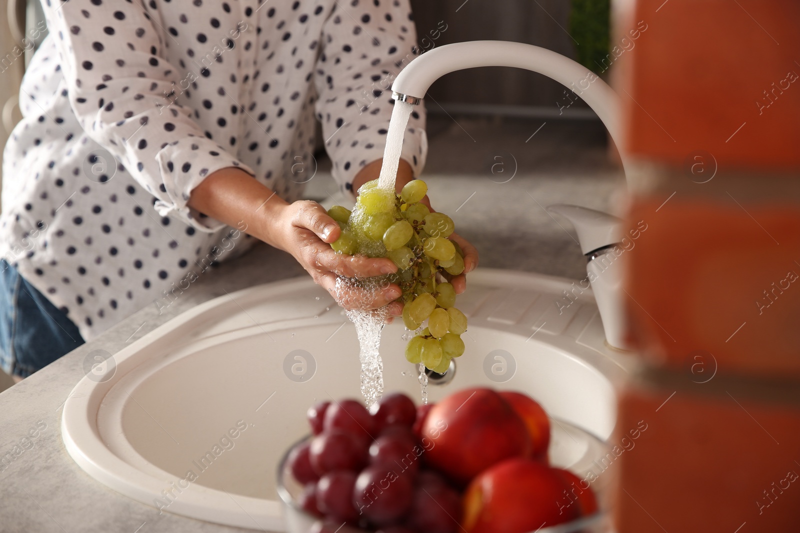 Photo of Woman washing fresh grapes in kitchen sink, closeup
