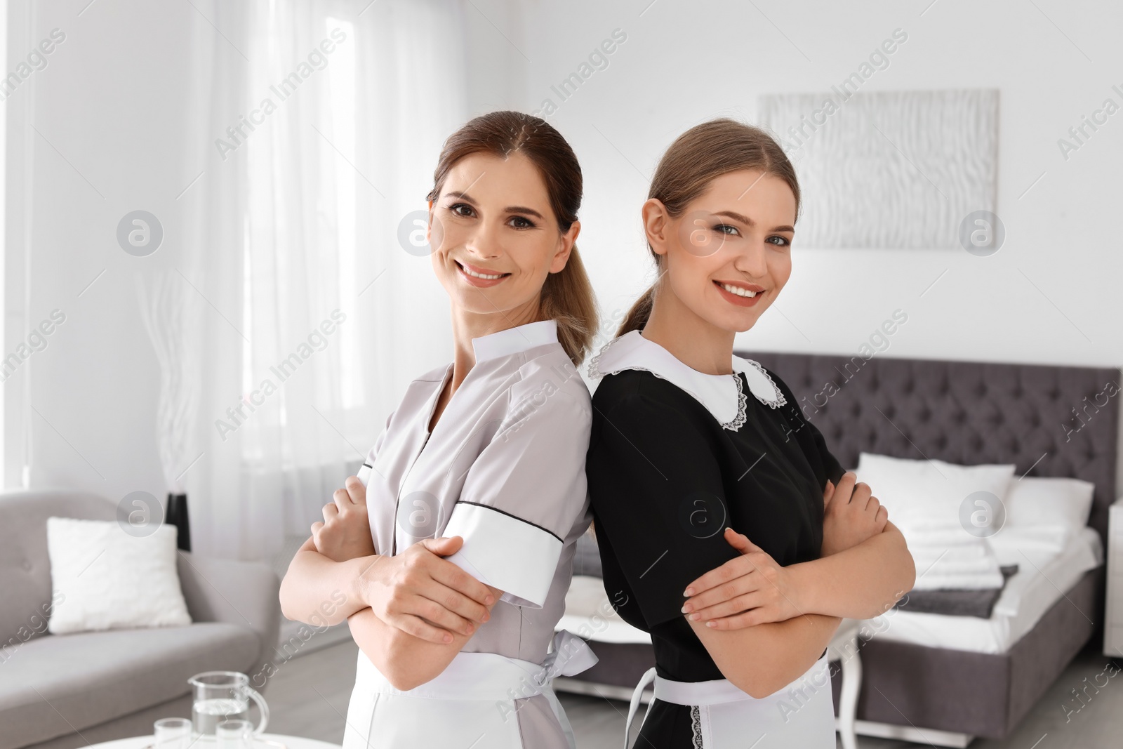 Photo of Professional chambermaids in uniform standing near bed indoors