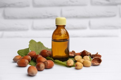 Photo of Bottle of hazelnut essential oil and nuts on white wooden table
