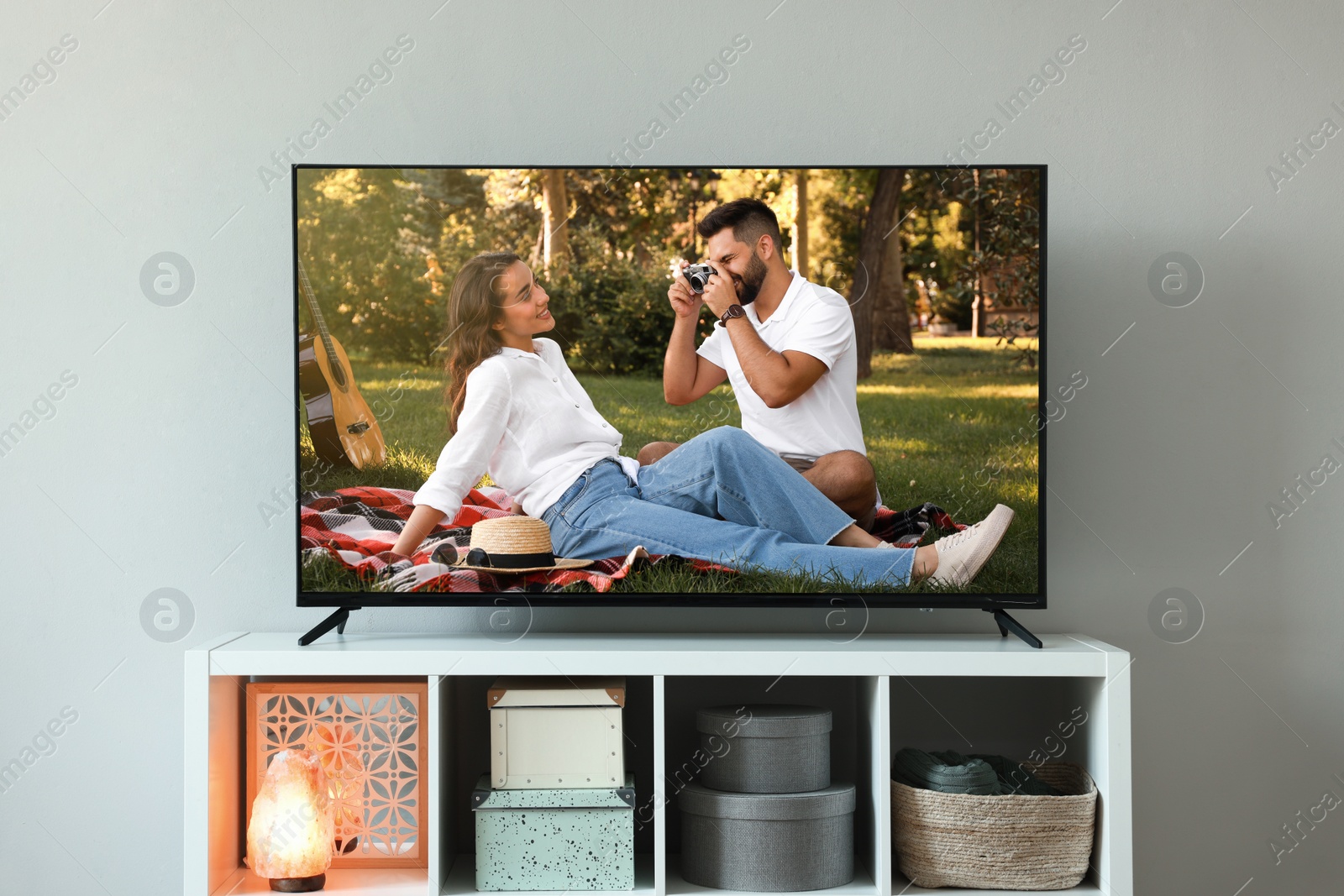 Image of Modern TV set on wooden stand in room. Scene of romantic movie on screen