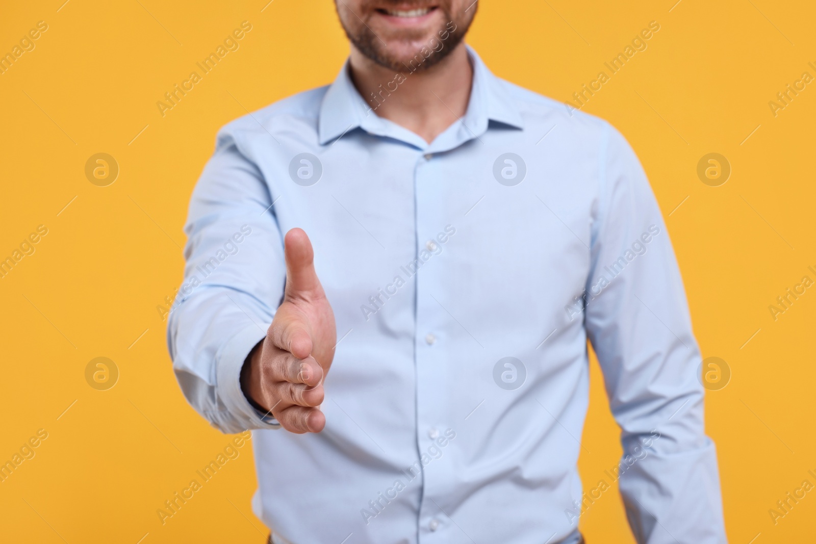 Photo of Man welcoming and offering handshake on yellow background, closeup